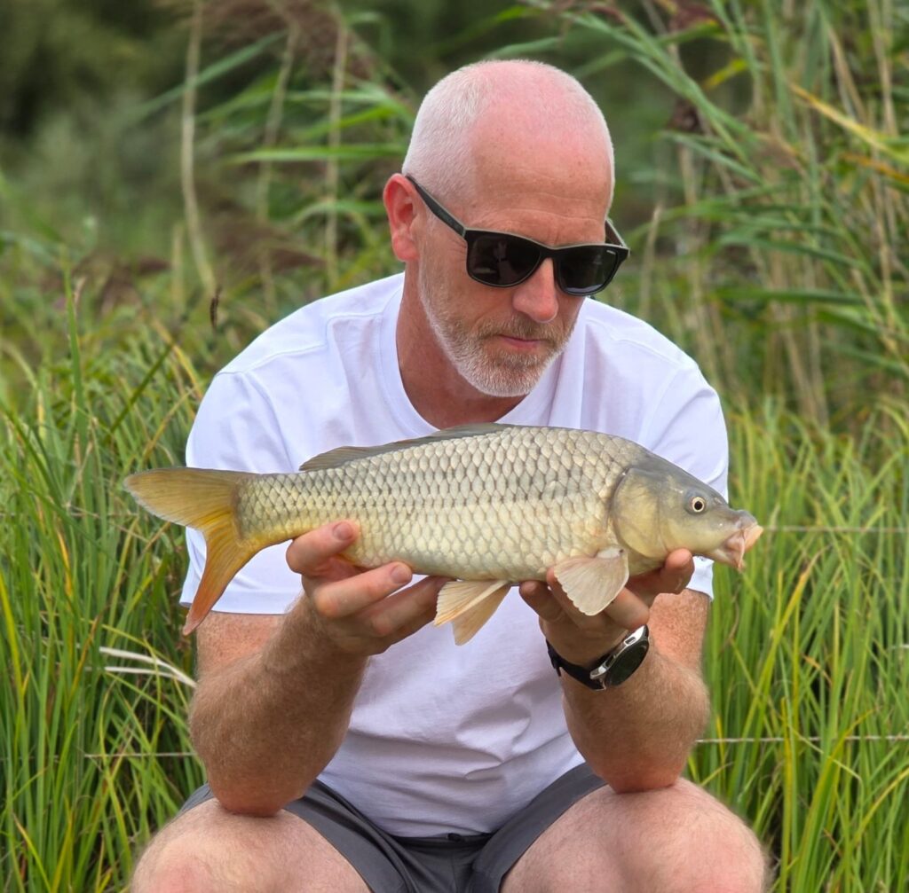 Angler holding a large common carp by the private fishing lake at Scotgate Cottage, Norfolk